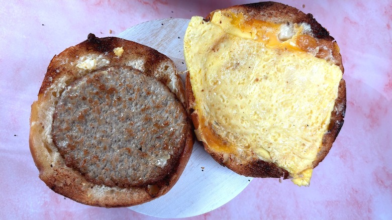 Overhead shot of open Panera Sausage & Egg Asiago Bagel Stack on white platform, pink marble background