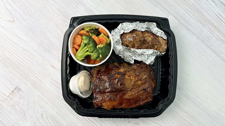 Texas roadhouse ribs, a baked potato and mixed vegetables in a black plastic container