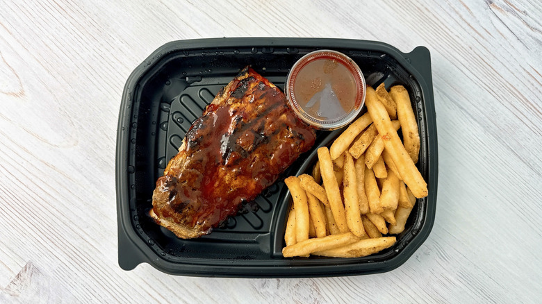 Longhorn steakhouse ribs, fries and pot of sauce in a black plastic container