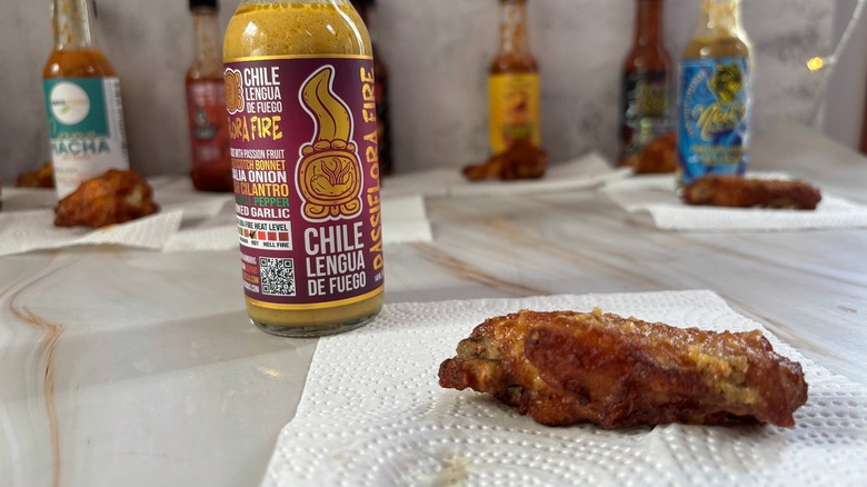 Bottle of Chile Lengua de Fuego Passiflora Fire hot sauce on table next to chicken wing