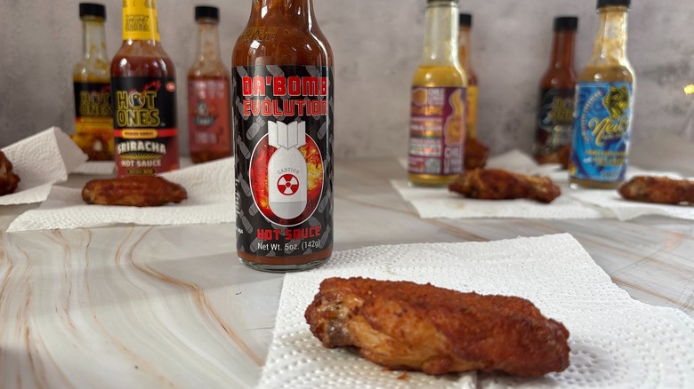 Bottle of Da'Bomb hot sauce on table next to chicken wing