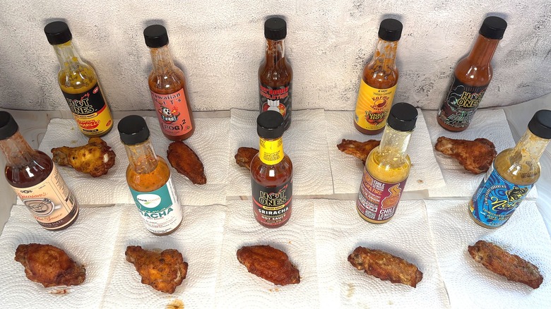Two rows of hot sauce bottles behind sauced wings on table