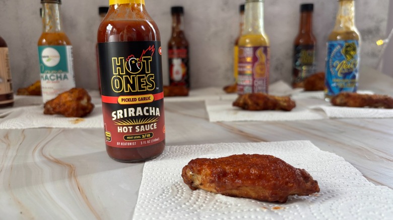 Hot Ones Pickled Garlic Sriracha hot sauce on table next to chicken wing