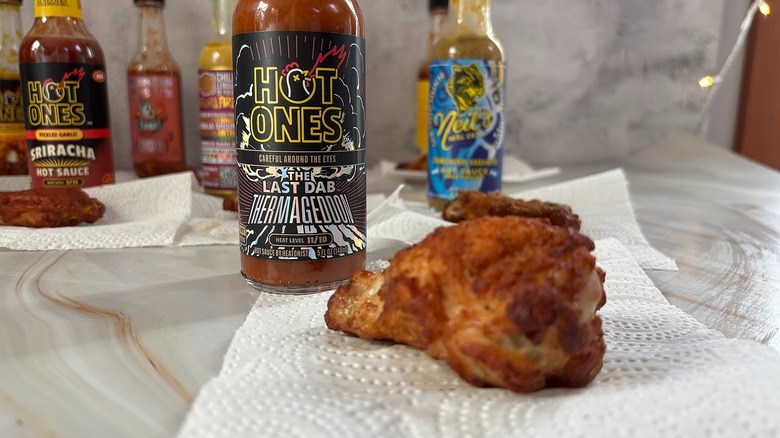 Bottle of The Last Dab Thermageddon hot sauce on table next to chicken wing