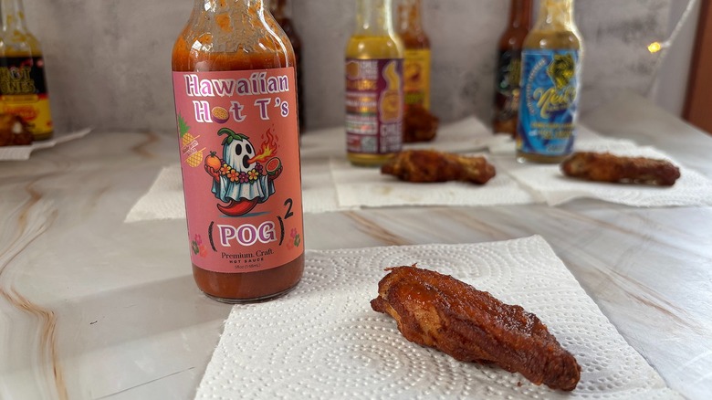 Bottle of POG Hawaiian Hot T's hot sauce on table next to chicken wing