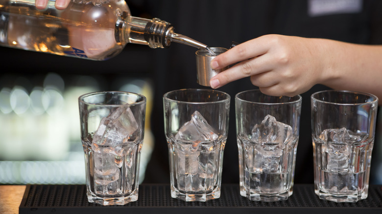 Someone pouring vodka into a shot glass above four glasses full of ice