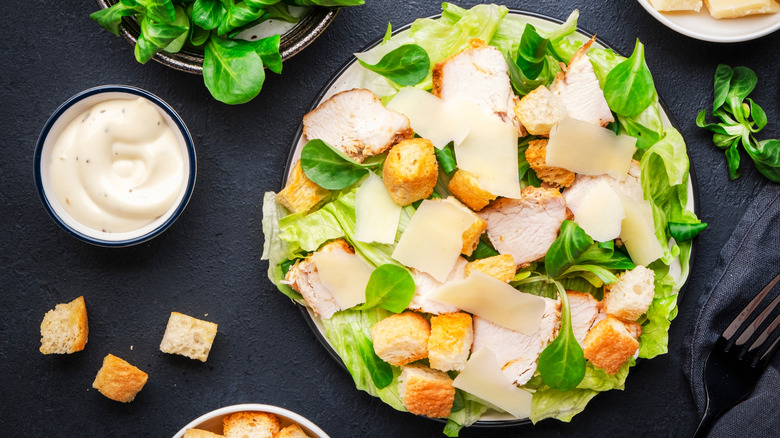 A classic Caesar salad with a pot of sauce and croutons