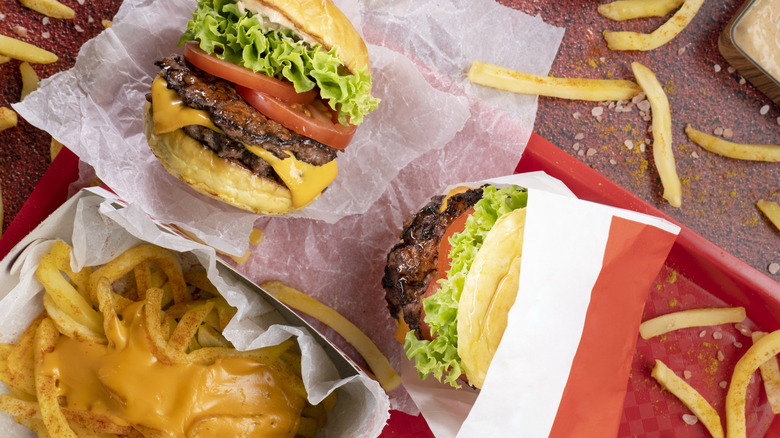 Fast food burgers and cheesy fries on red plastic tray