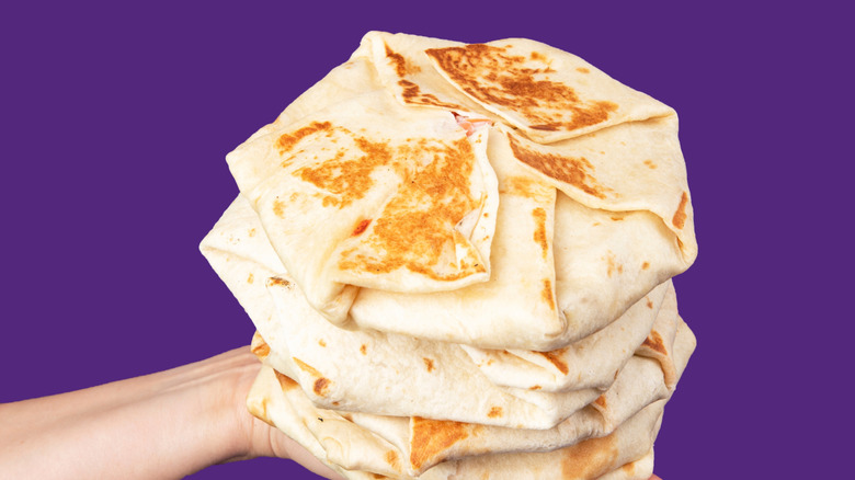 Hand holding stack of Crunchwrap Supremes on purple background