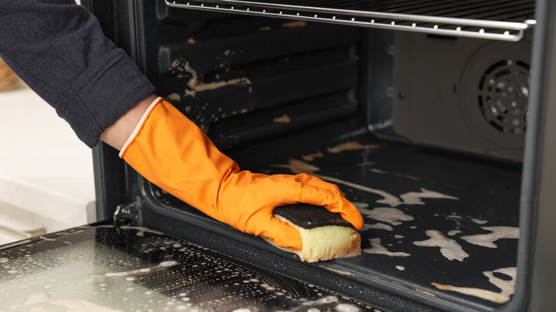 Someone in a rubber glove using a sponge to clean the bottom of an oven