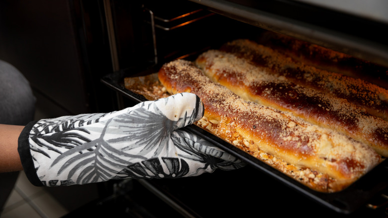 Close-up of person removing tray of broiled baked goods from the oven