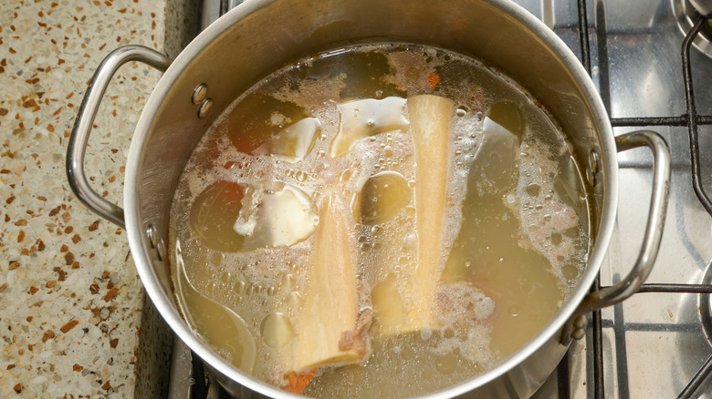 Two bones cooking in a large pot with lots of fat visible on the surface of the broth