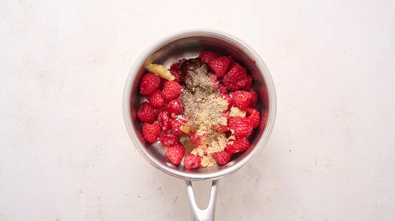 A small pot filled with bright raspberries, brown sugar, and seasonings