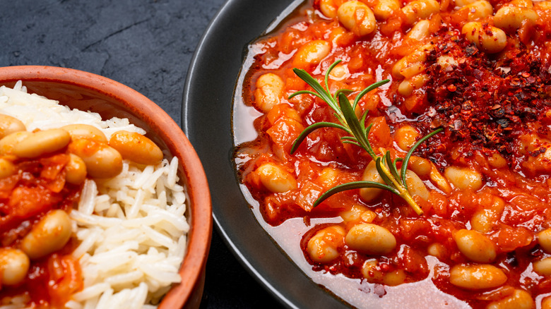 A close up of a plate of baked beans on a plate, next to a bowl of beans on top of rice.