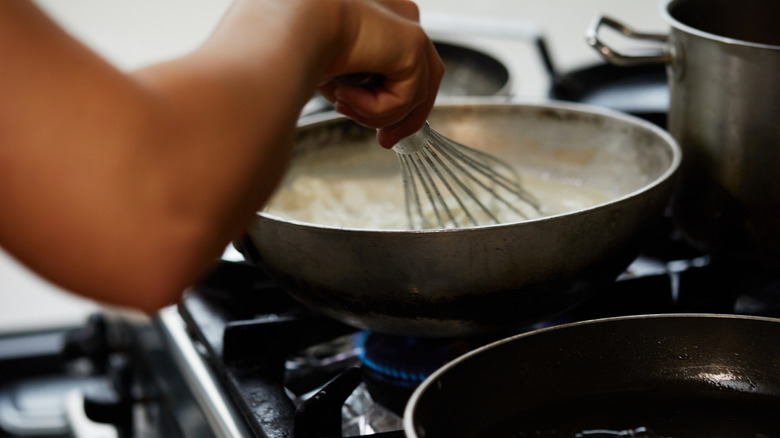 A person is whisking gravy in pan on the stove.
