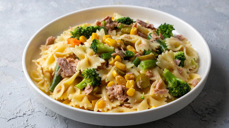A white bowl of tuna pasta salad with broccoli, corn, and olives