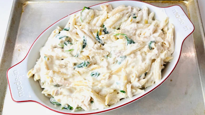 an unbaked ceramic dish of chicken alfredo pasta sitting on a metal sheet pan