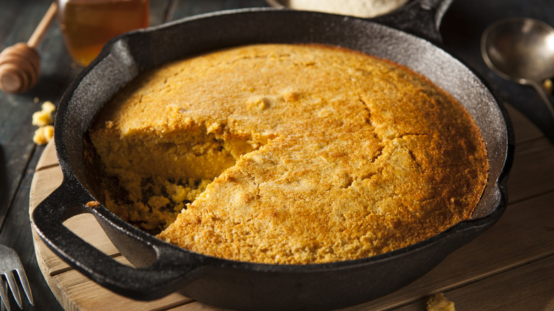 A cast iron skillet full of cornbread, with a single slice removed.