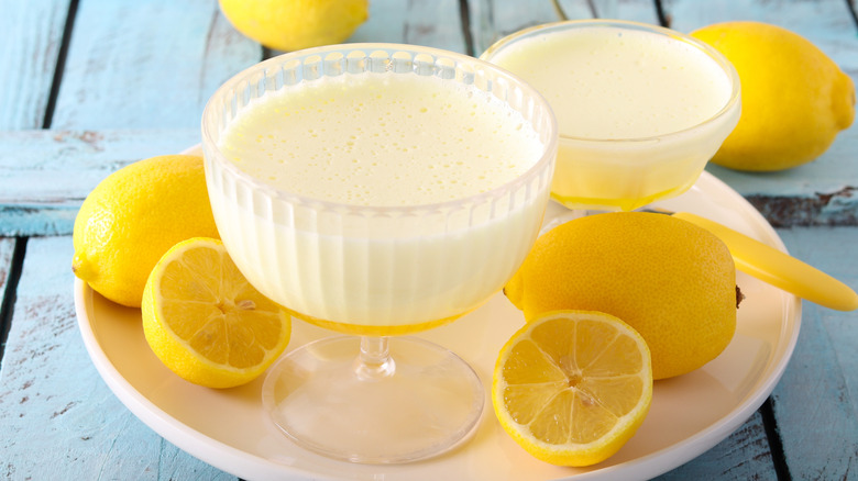 Glass bowls of lemon mousse with whole and halved lemons on plate, resting on blue wooden table