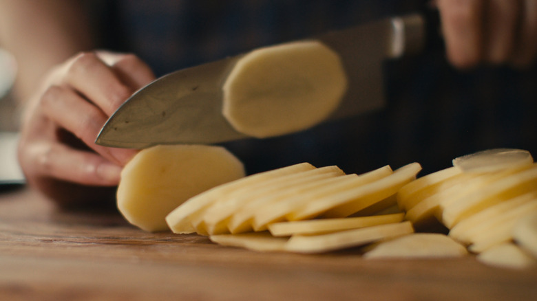A person thinly slices potatoes on a chopping board
