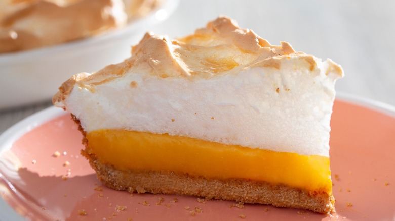 A slice of orange pie with a graham cracker crust and meringue topping on a pink plate