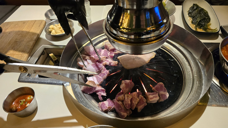 Chef using scissors and tongs to cut meat at Korean BBQ restaurant