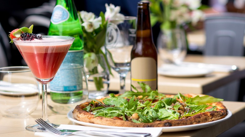 Italian outdoor table with pizza, strawberry cocktail, and bottles of beer and sparkling water