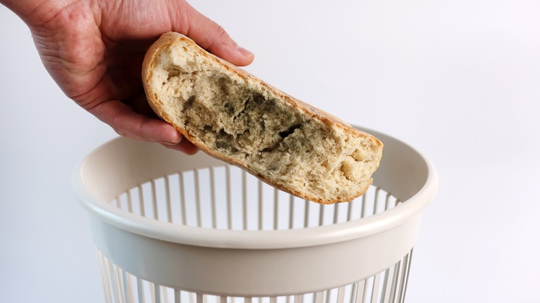 A person tossing out a loaf of molded bread