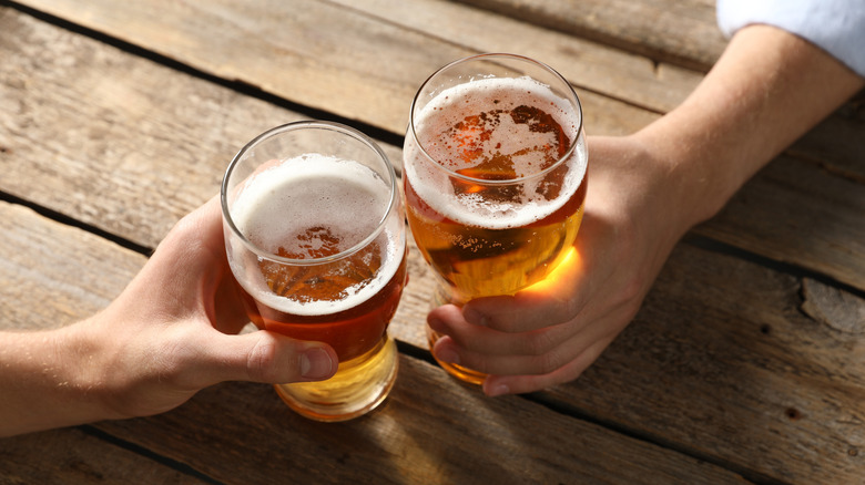 Two hands holding beer glasses together on table