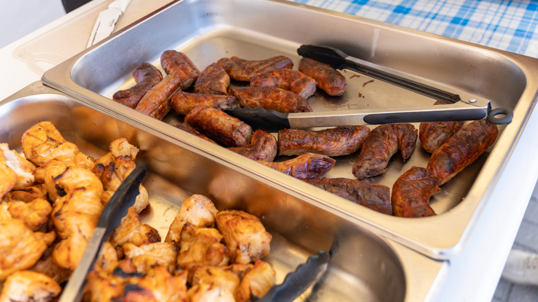 Buffet trays full of sausage and chicken with tongs in each one