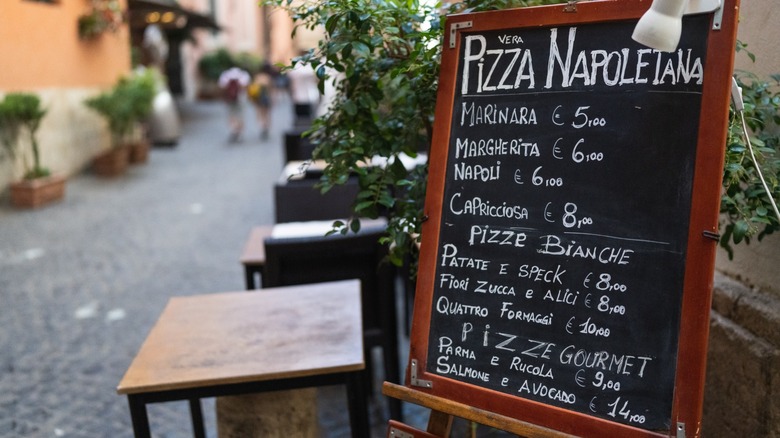 A pizza restaurant menu written in chalk on a blackboard on the side of the street in Rome. The menu is in Italian