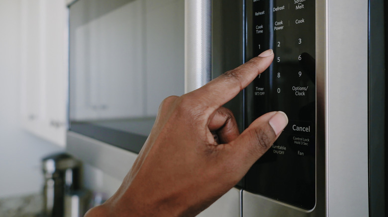 Hand pressing a number button on a microwave oven