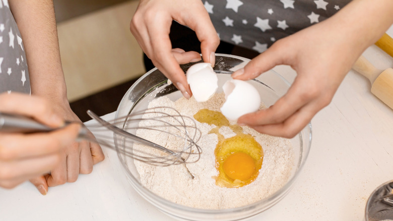 People mixing eggs into a bowl of batter