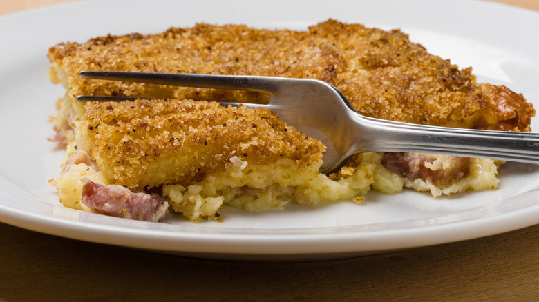 A fork digging into a portion of a crusty coated potato casserole