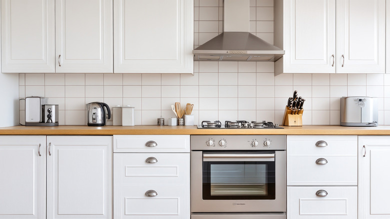White kitchen with stainless steel appliances, white cabinets, and light wood floors in Montreal