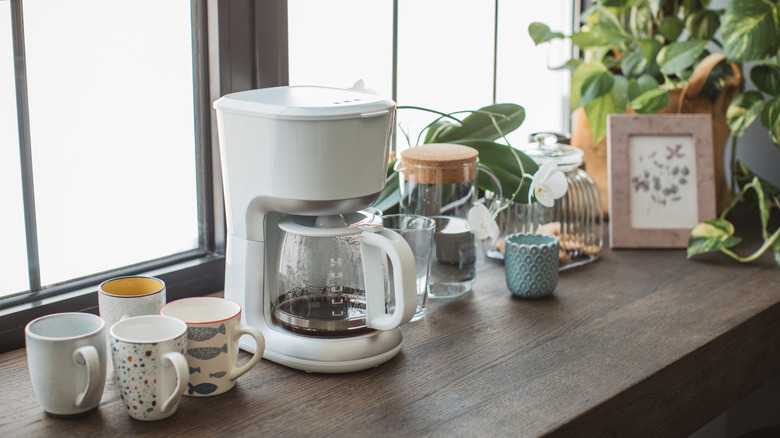 cluttered kitchen counter with coffee maker and mugs