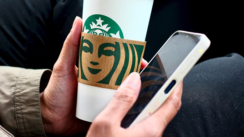 Starbucks hot cup with person holding phone
