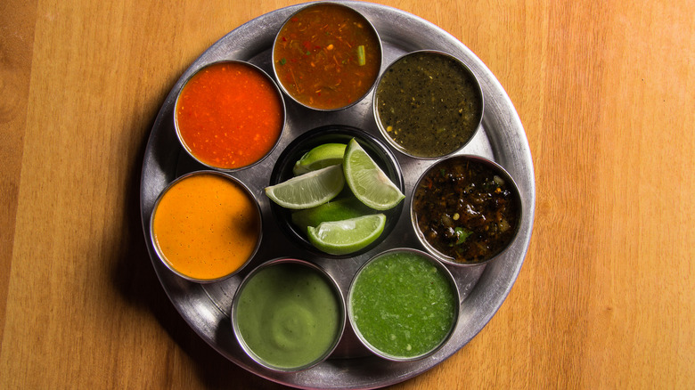various salsas in small metal bowls on a plate with limes