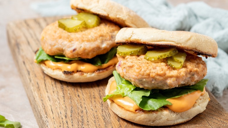 A pair of salmon burgers on English muffins with lettuce, pickles, and an orange sauce