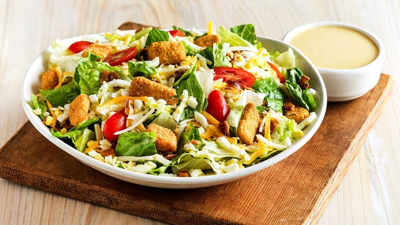 The Outback Steakhouse Aussie Cobb salad in a white bowl next to a side dish of Ranch dressing