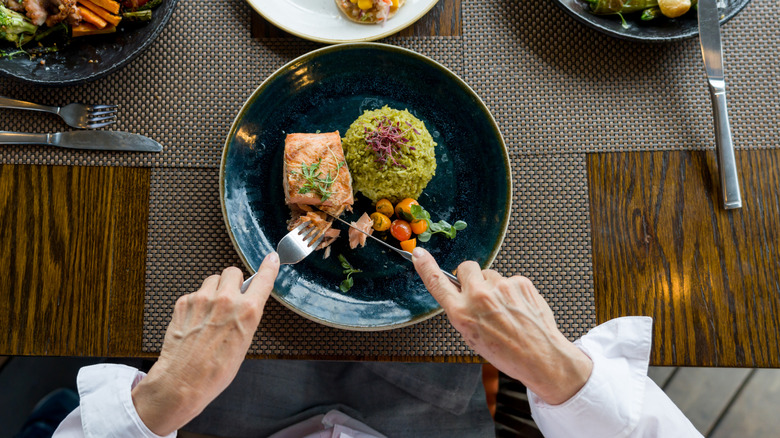 A diner cuts into a meal featuring salmon