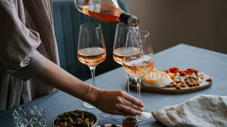 A person pouring a bottle of rosé wine into long-stemmed glasses