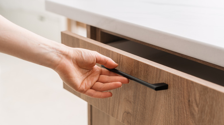Cropped shot of woman hand opening a wooden drawer in a contemporary kitchen.