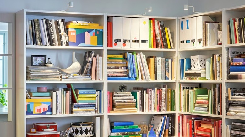 A wall of white BILLY bookcases filled with colorful books, storage boxes, and decorative objects, creating a vibrant and organized focal point in a cozy living space.