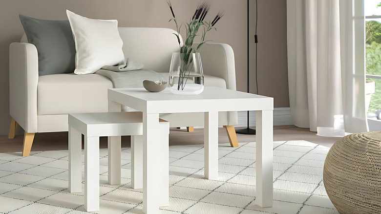 A set of white LACK tables with a glass vase centerpiece, standing in front of a cozy white sofa
