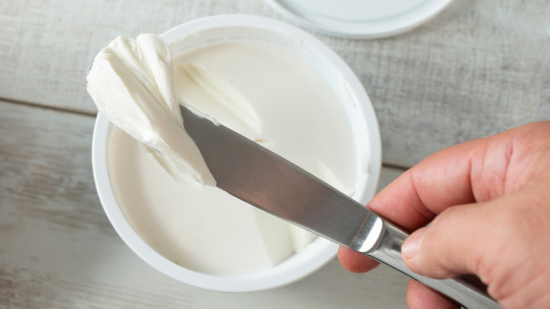 Cream cheese with a knife being held by a hand
