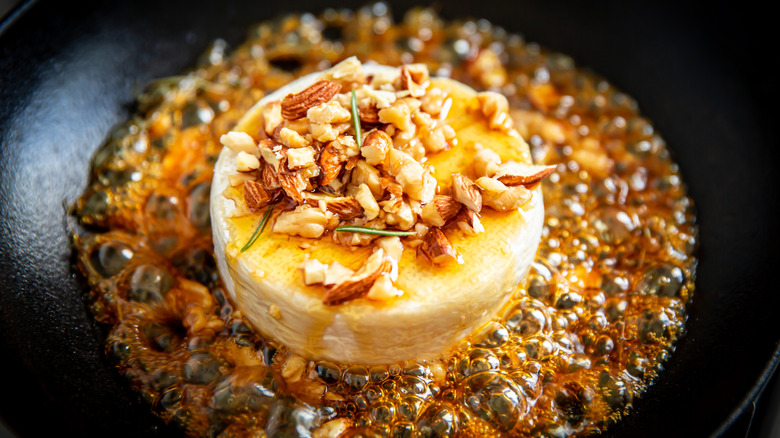 Nut-topped Brie cooking in bubbly sugar in black pan