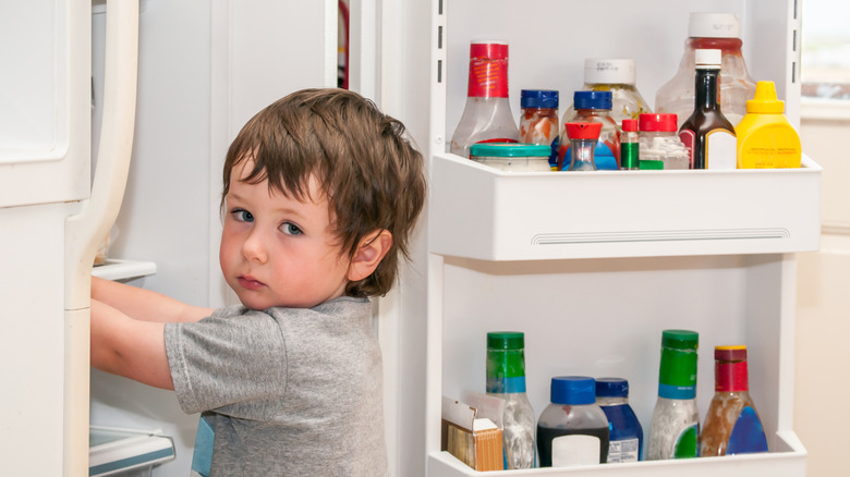 kid getting in fridge with condiments in the door