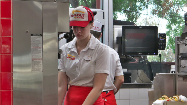 Female In-N-Out employee wearing a white blouse, red apron, and a branded baseball hat