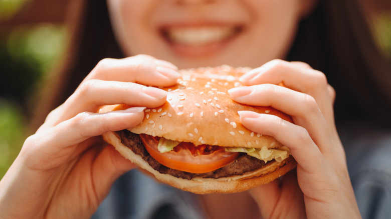 Person smiling holding burger in hand